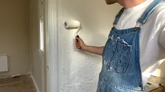 Mann streicht weiße Wand mit Farbroller in hellem Raum